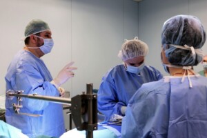 Ķirurgi operāciju zālē, valkājot medicīniskās drēbes un maskas, veic operāciju.
