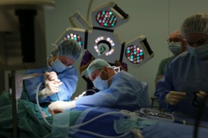 Divi ķirurgi veic operāciju, izmantojot medicīniskos instrumentus, apgaismojumu un sterilus apģērbus.