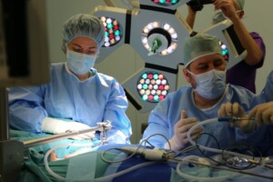 Divi ķirurgi veic operāciju, valkājot medicīniskās drēbes un maskas, apgaismojums operāciju zālē.