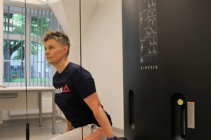 Sieviete vingro ar Kinesis trenažieri Rīgas 1. slimnīcā, izmantojot stieņus un siksnas.