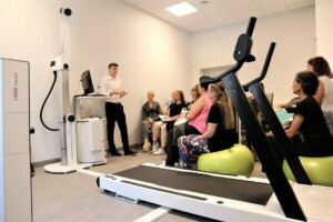 Rīgas 1. slimnīcā notiek prezentācija par rehabilitāciju, redzams lektors un klausītāji. Ierīces: DIERS.