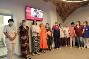 Rīgas 1. slimnīcas darbinieki stāv grupā, fona ekrānā redzama informācija par bērnu rehabilitāciju.