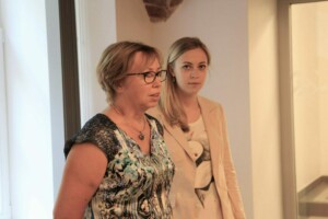 Divas sievietes runā Rīgas 1. slimnīcā, viena no tām ir ar brillēm un ziedu raksta blūzi.