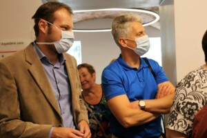 Divi vīrieši un sieviete gaida Rīgas 1. slimnīcas uzgaidāmajā zonā, visi ar sejas maskām.