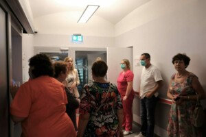 Grupa cilvēku, tostarp mediķi, gaida pie pacienta istabas Rīgas 1. slimnīcā. Redzami numuri 121.