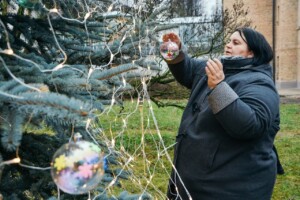 Sieviete rotā Ziemassvētku eglīti ar rotājumiem un gaismiņām Rīgas 1. slimnīcas pagalmā.