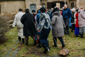 Grupa cilvēku dodas pa taku, apģērbi ir dažādi, daži nēsā mēteles un zābakus. Rīgas 1. slimnīca.