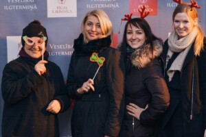 Četras sievietes pozē ar aksesuāriem uz fona ar tekstu "Veselībai ilgtermiņā" un "Rīgas 1. slimnīca".