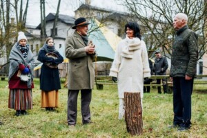 Cilvēki sarunājas ārā, pie koka stumbra, Rīgas 1. slimnīcas pasākumā. Apkārt redzami koki un teltis.