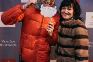 Divi cilvēki pozē fotogrāfijā ar aksesuāriem, fons ar tekstu "Veselībai ilgtermiņā" un "Rīgas 1. slimnīca".
