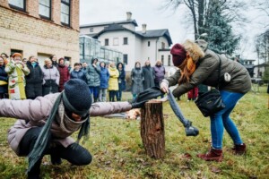 Divas sievietes piedalās aktivitātē ārā, apkārt stāv skatītāji, fonā redzama uguns. Rīgas 1. slimnīca.