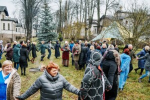 Cilvēki dejo un turas rokas, svinot kopā Rīgas 1. slimnīcas pasākumā ārā. Redzams ugunskurs.
