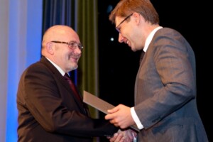 Divi vīrieši sveicina viens otru, pasniedzot balvu Rīgas 1. slimnīcas pasākumā.