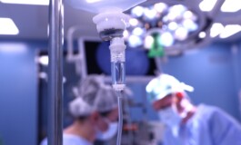Infūzijas sistēma operāciju zālē, fona attēlā redzami medicīnas darbinieki. Rīgas 1. slimnīca.