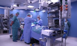 Operāciju telpa ar medicīnas personālu, aprīkojumu un pacientu uz operāciju galda.