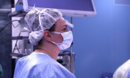 Sieviete medicīnas tērpā un maskā, stāvot operāciju telpā Rīgas 1. slimnīcā.